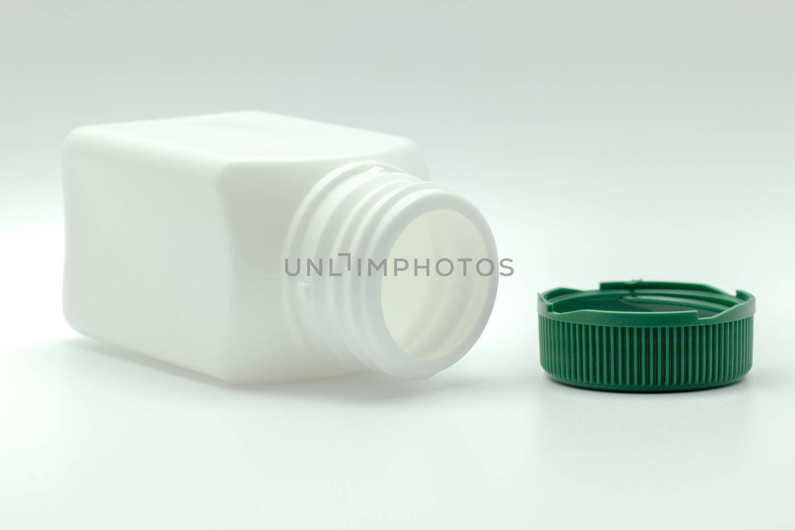 White bottle of antibiotic and green bottle cap placed on a whit by SaitanSainam