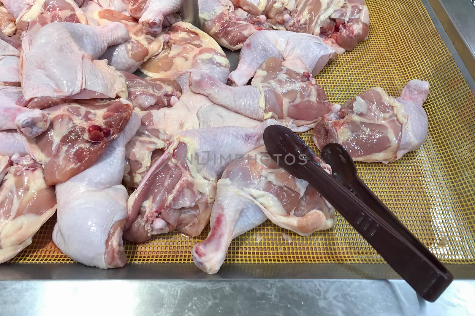 Raw chicken of drumstick on the yellow container and the tongs by TakerWalker