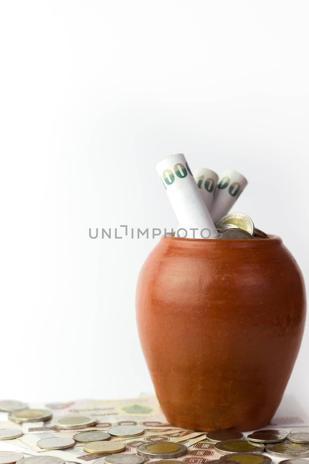 Banknotes are rolled into pot or jar is a kind of pottery and coins are stacked on the white background. The concept of business and save money for a good future.
