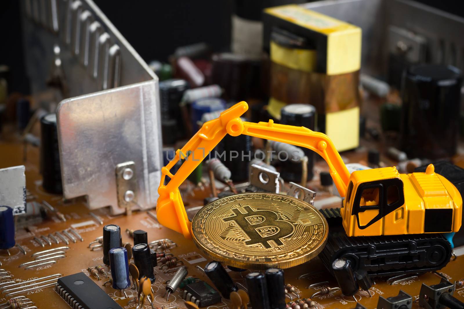 Backhoe dig bitcoin on mainboard. Concept of bitcoin mining business.