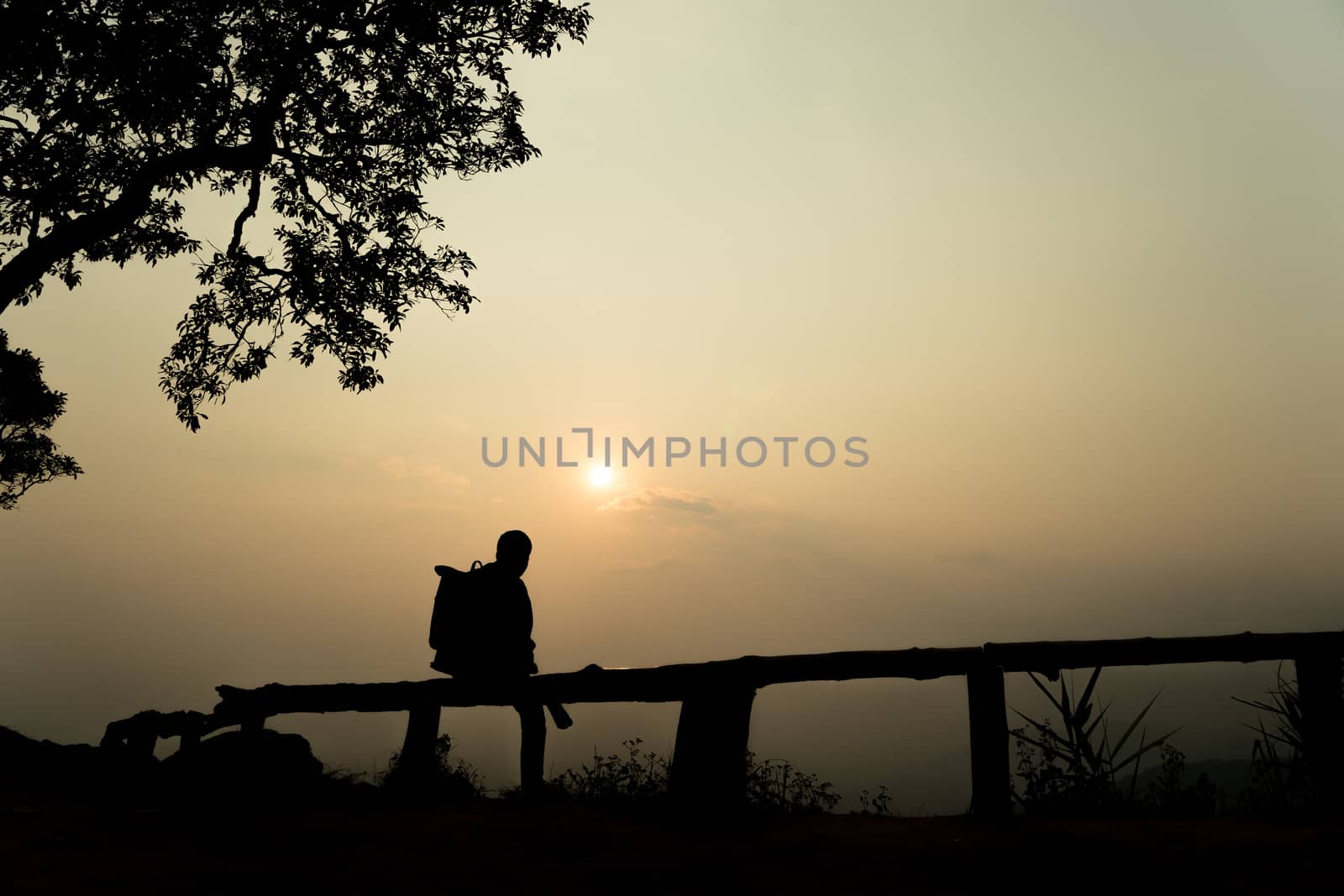 Silhouette lonely men sitting at the view point watching the sunset go down in among the mountains on evening.