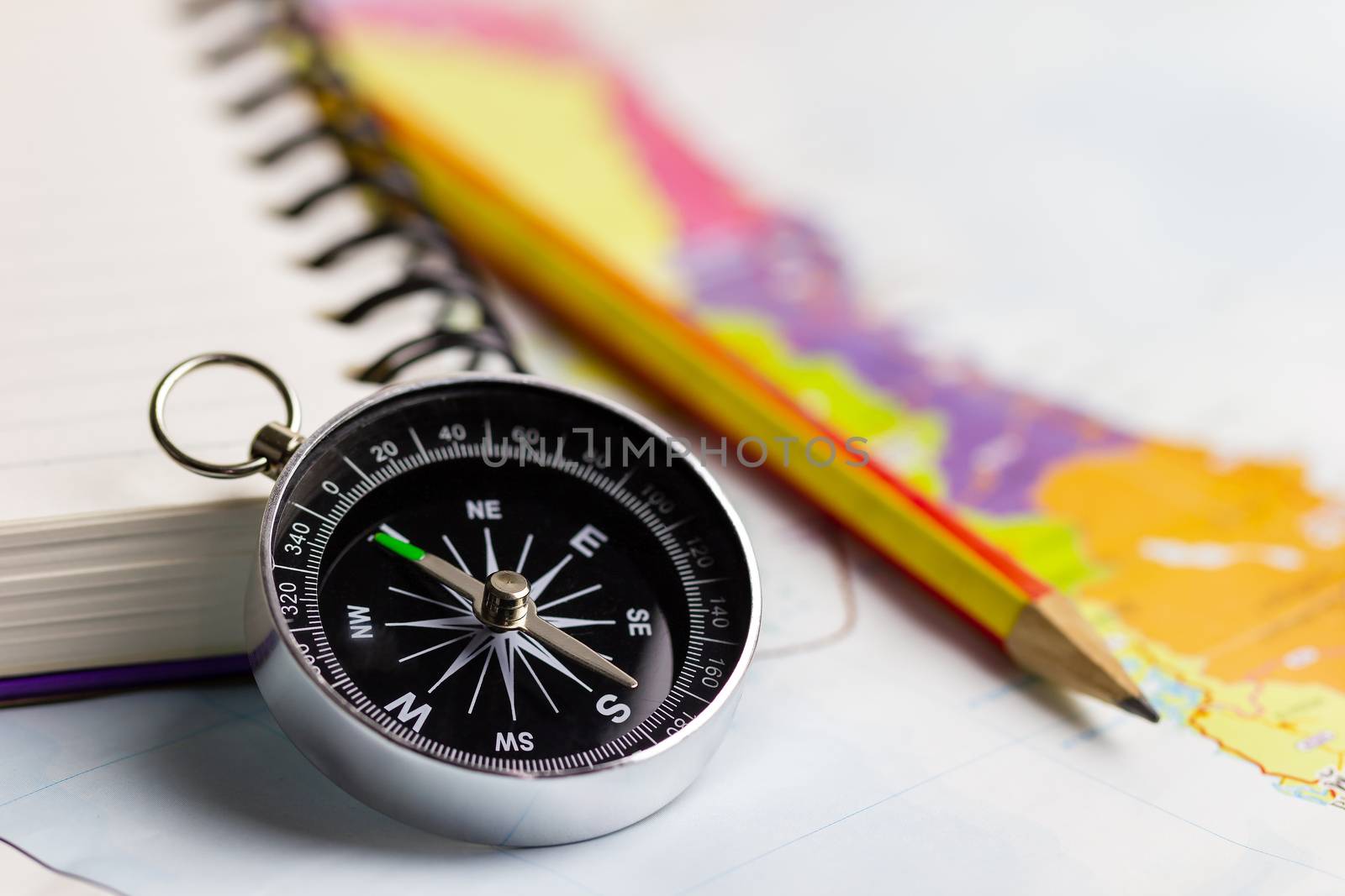 Compass notebook and pencil laid on a paper map. The concept record of travel.