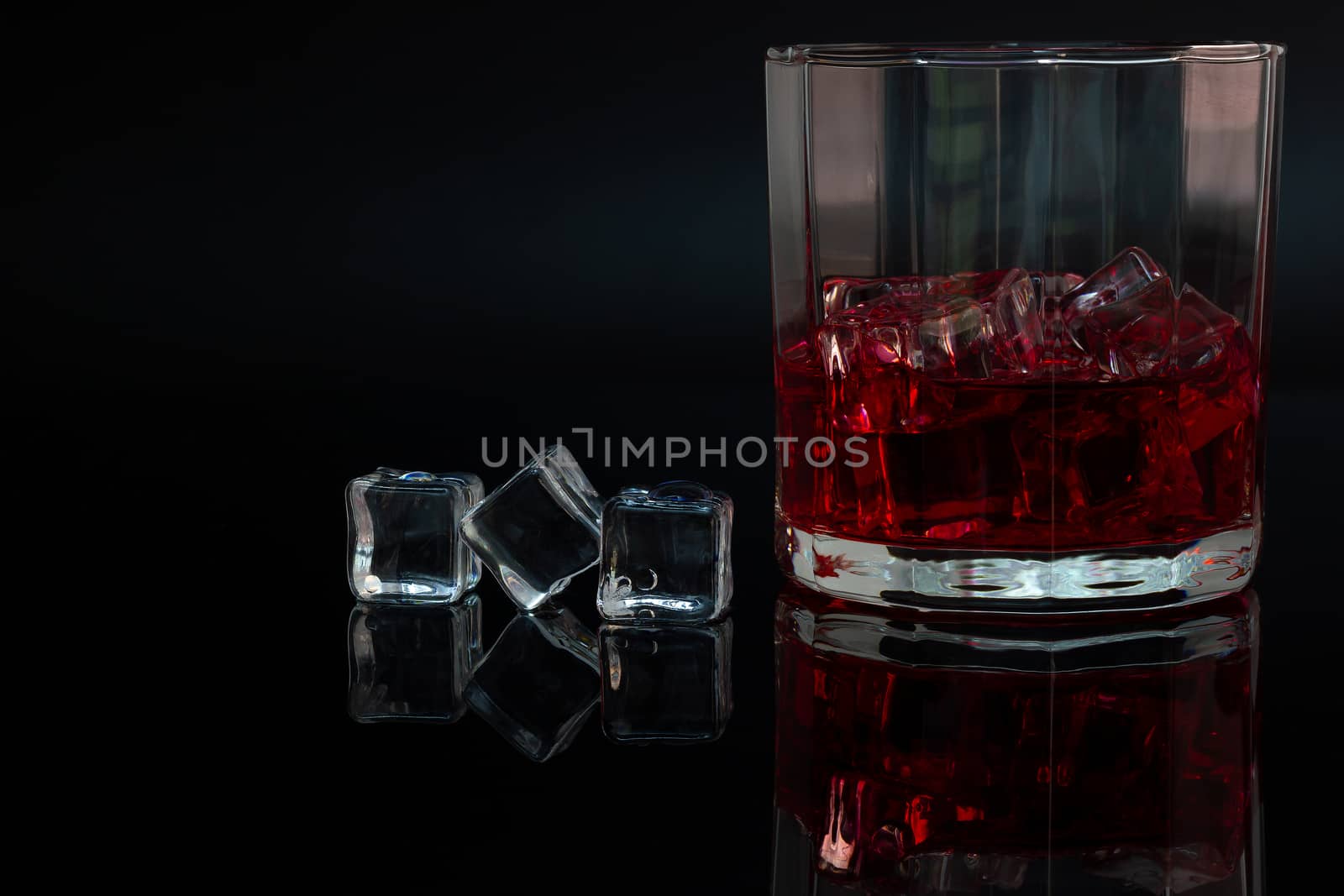 Polygon glass and reflection of liquor and ice on dark background.