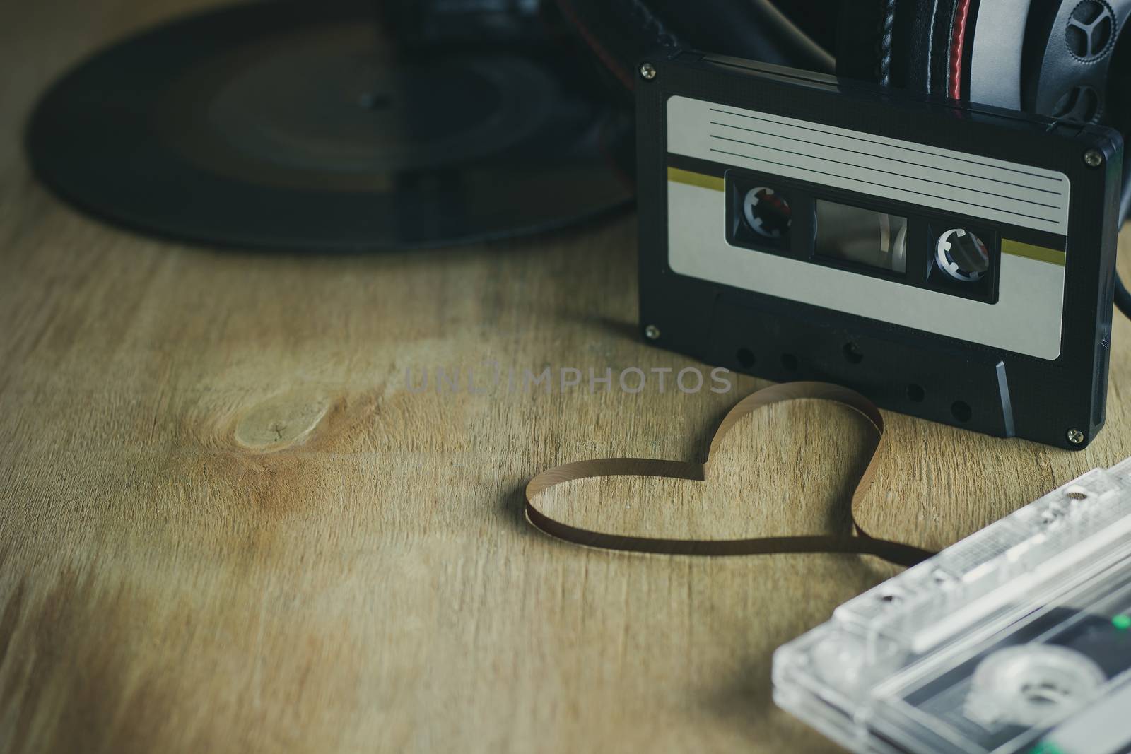 Cassette heart shaped tapes and headphone with gramophone record platter on wood background. The concept of love in music.
