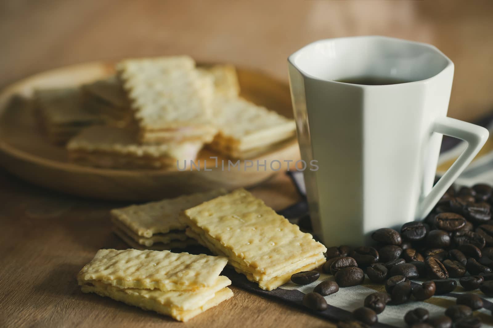 Crackers are placed on wooden plates and coffee cup with roasted coffee beans on a brown table.