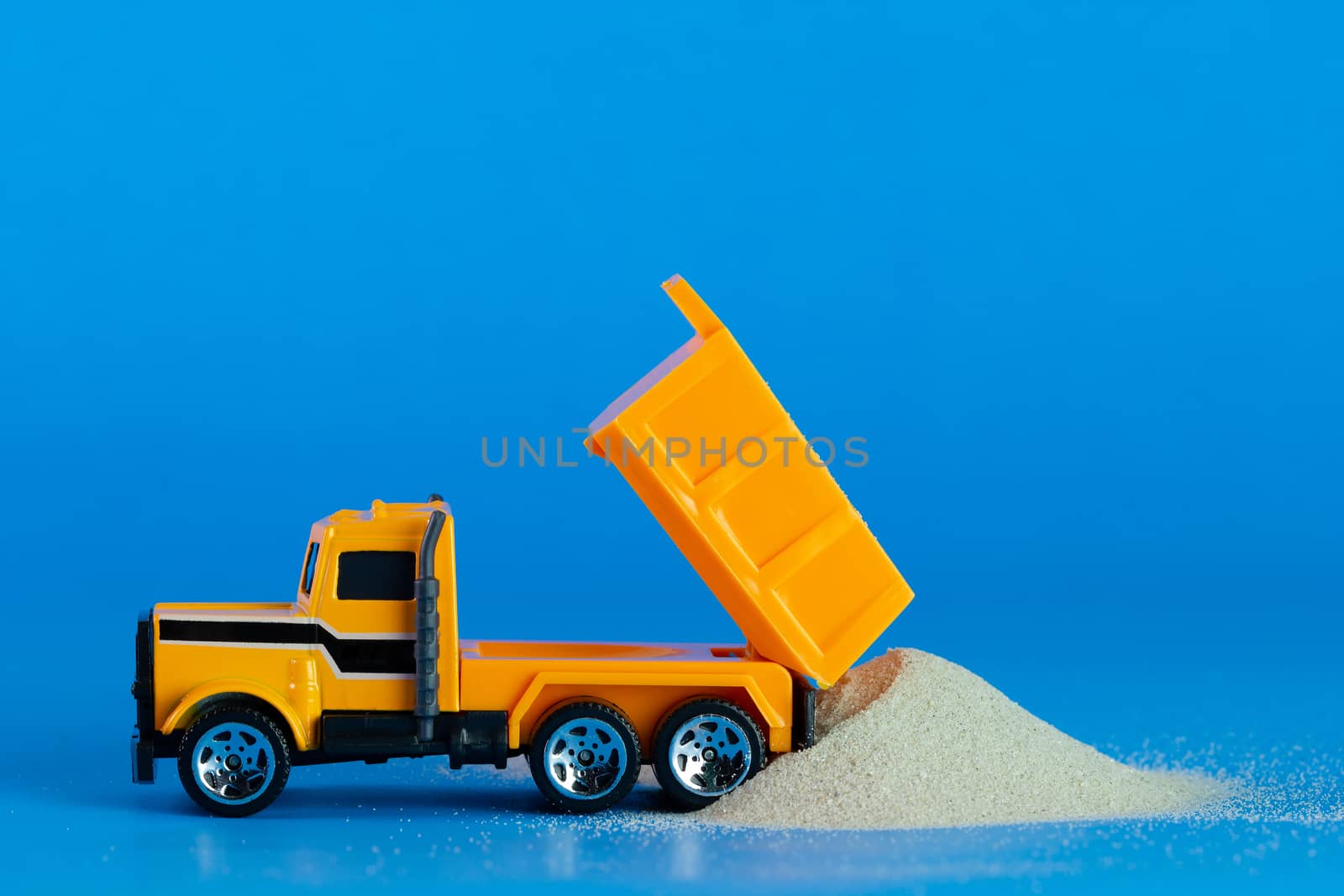 Yellow toy truck is pouring sand on the blue background. Concept of construction.