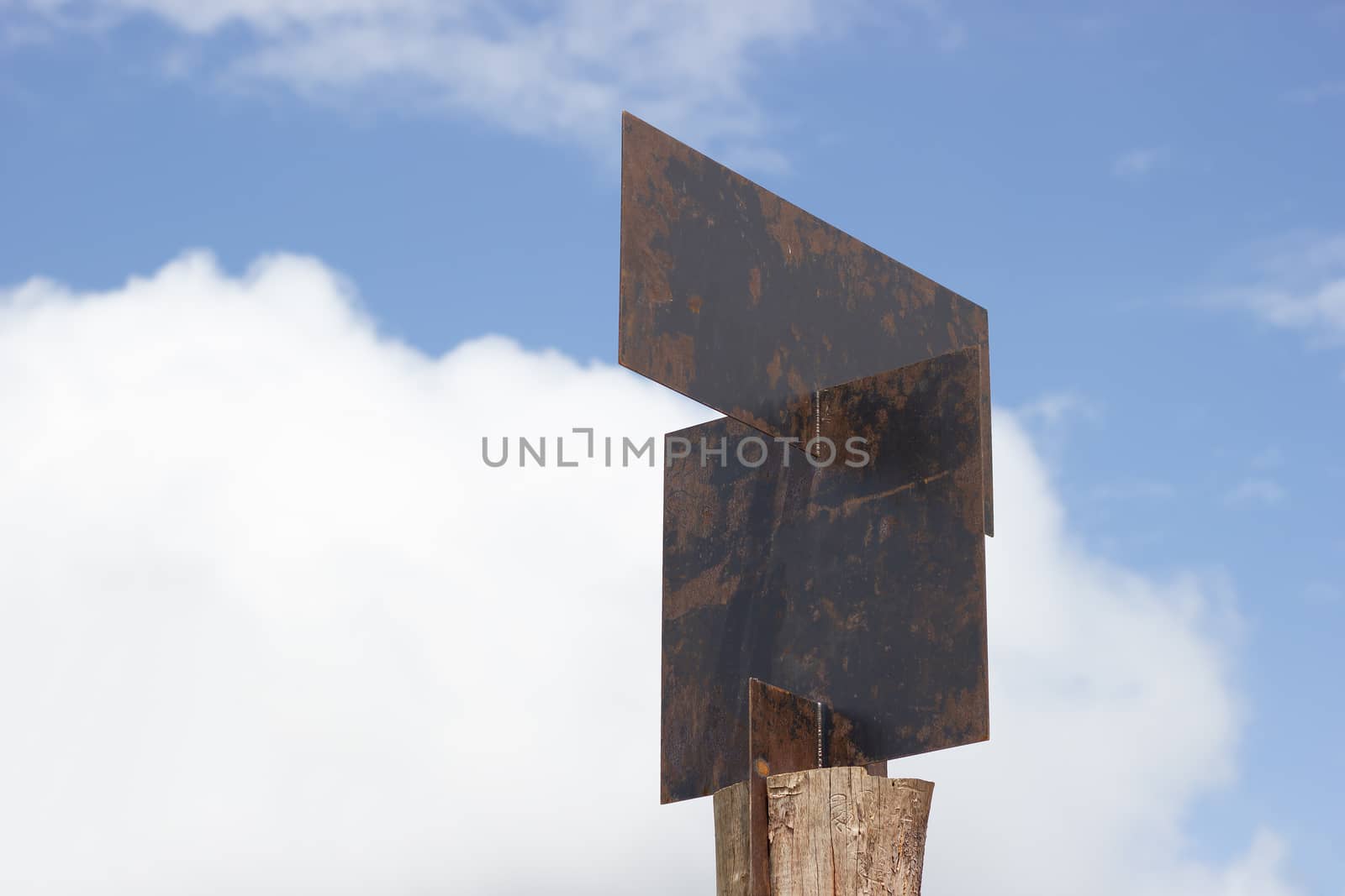 Blank guide post made of steel plates are pinned on wooden posts on sky background.