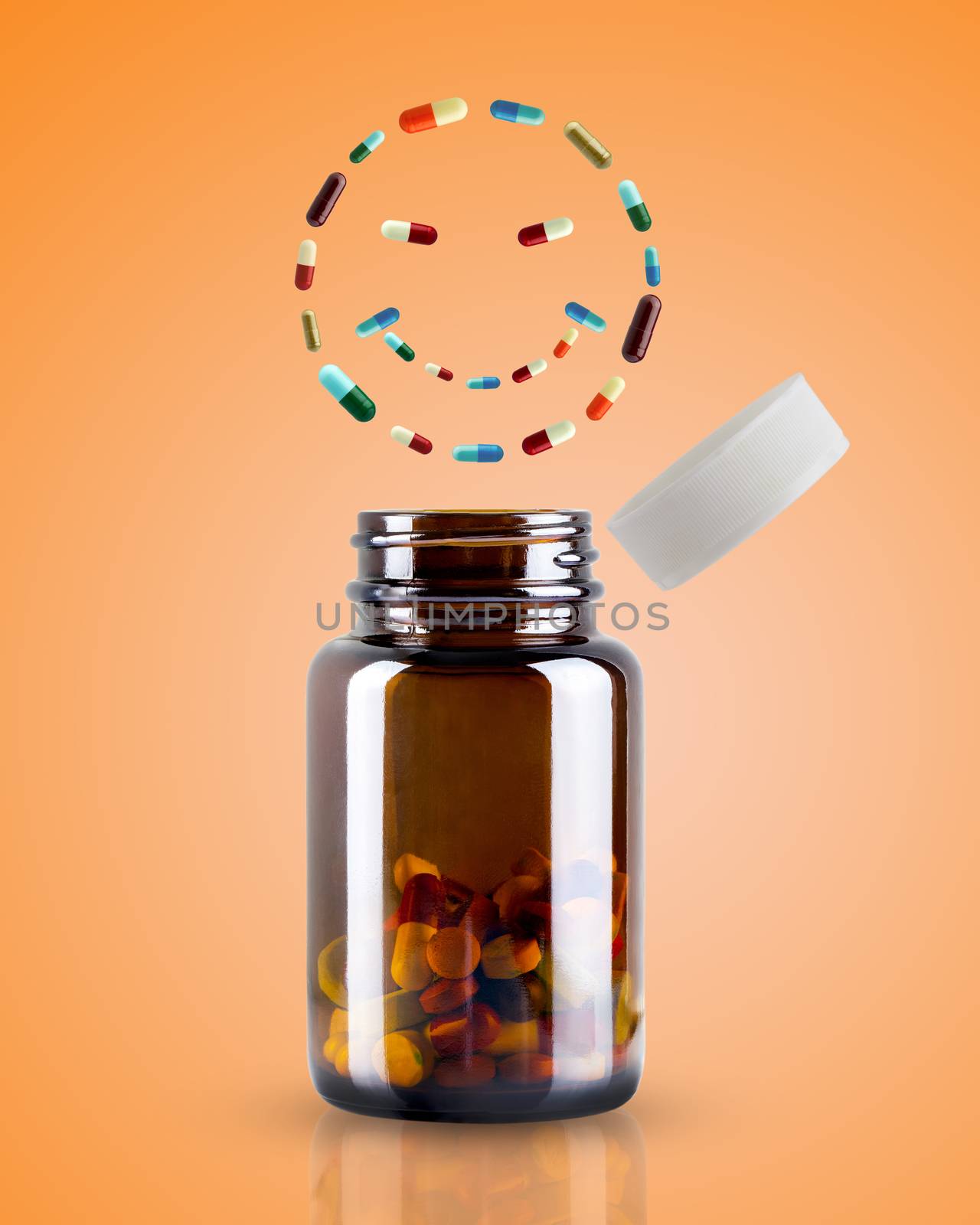 The medicine bottle is opened and the pill is floating in the shape of smiley on orange background. Concept of health care.