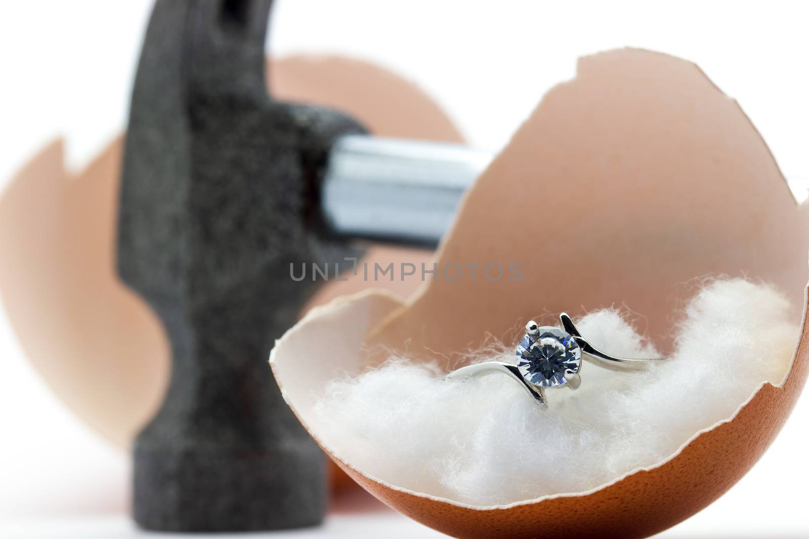 The egg shell is broken by a hammer and fake diamond ring in the egg shell on white background. Concept of birth or beginning a married life.