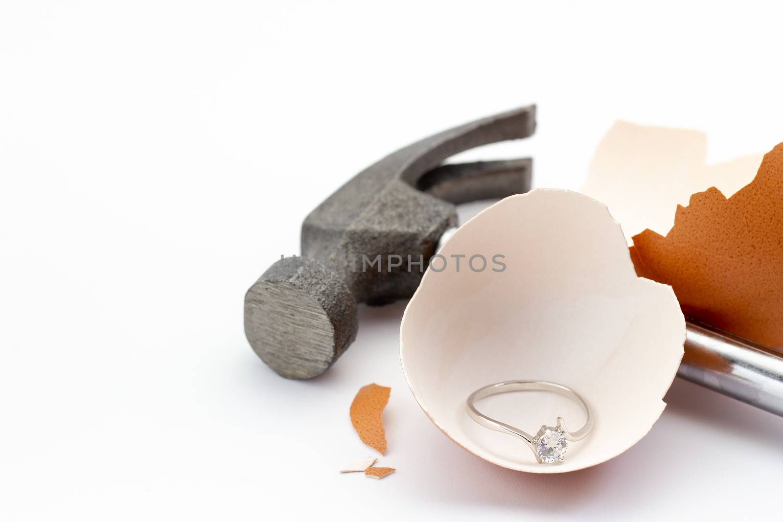 The egg shell is broken by a hammer and fake diamond ring in the egg shell on white background. Concept of birth or beginning a married life.