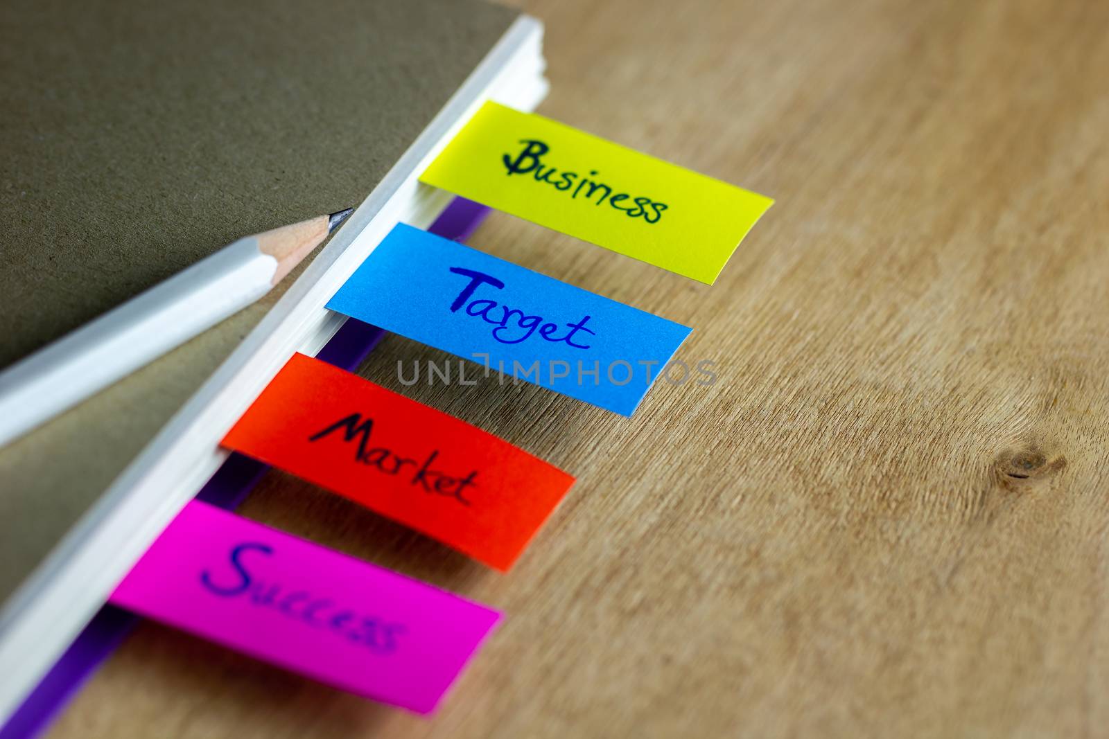 Colorful bookmarks are written for business, target, market, success, and have a white pencil put on a brown book cover. Concept of business.