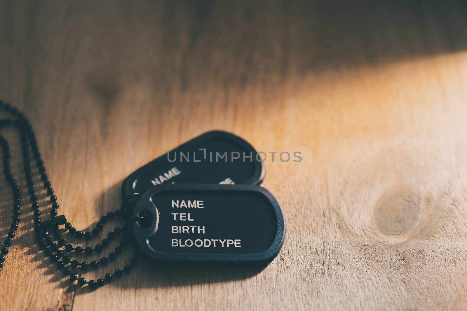 Soldier tag or dog tag laid on brown wooden table and sunlight.