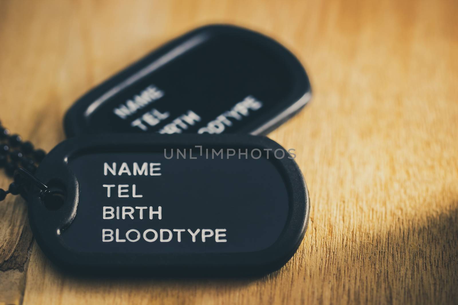 Soldier tag or dog tag laid on brown wooden table with stone and morning sunlight.