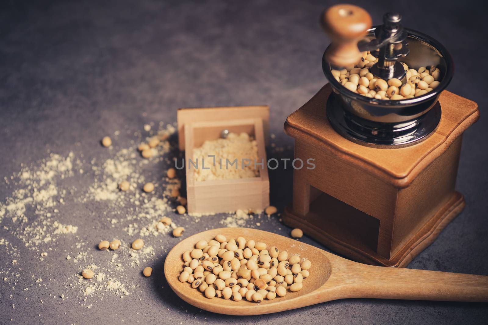 Coffee grinder grinding soybeans into powder and wooden ladle in darkness. Used to make soy milk.