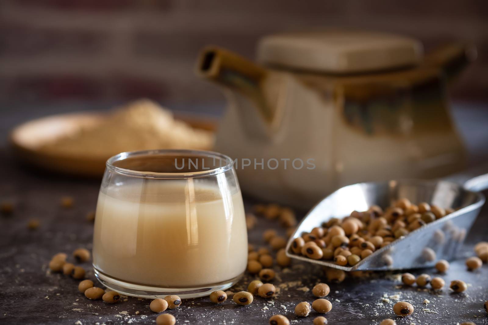 Soymilk in the glass and the kettle is placed beside. Soybean powder is crushed in a wooden dish and has scattered soy beans on the table in morning light.