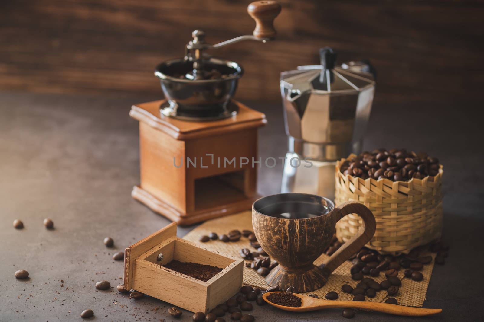 Brew black coffee in coconut cup and morning lighting. Roasted coffee beans in a bamboo basket and wooden spoon. Vintage coffee grinder and moka pot. Concept of coffee time in morning or start the new day.