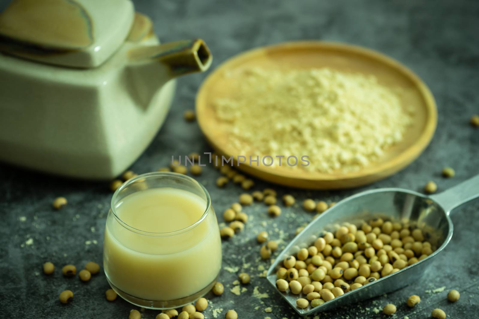 Soymilk in the glass and the kettle is placed beside. Soybean powder is crushed in a wooden dish and has scattered soy beans on the table in morning light.