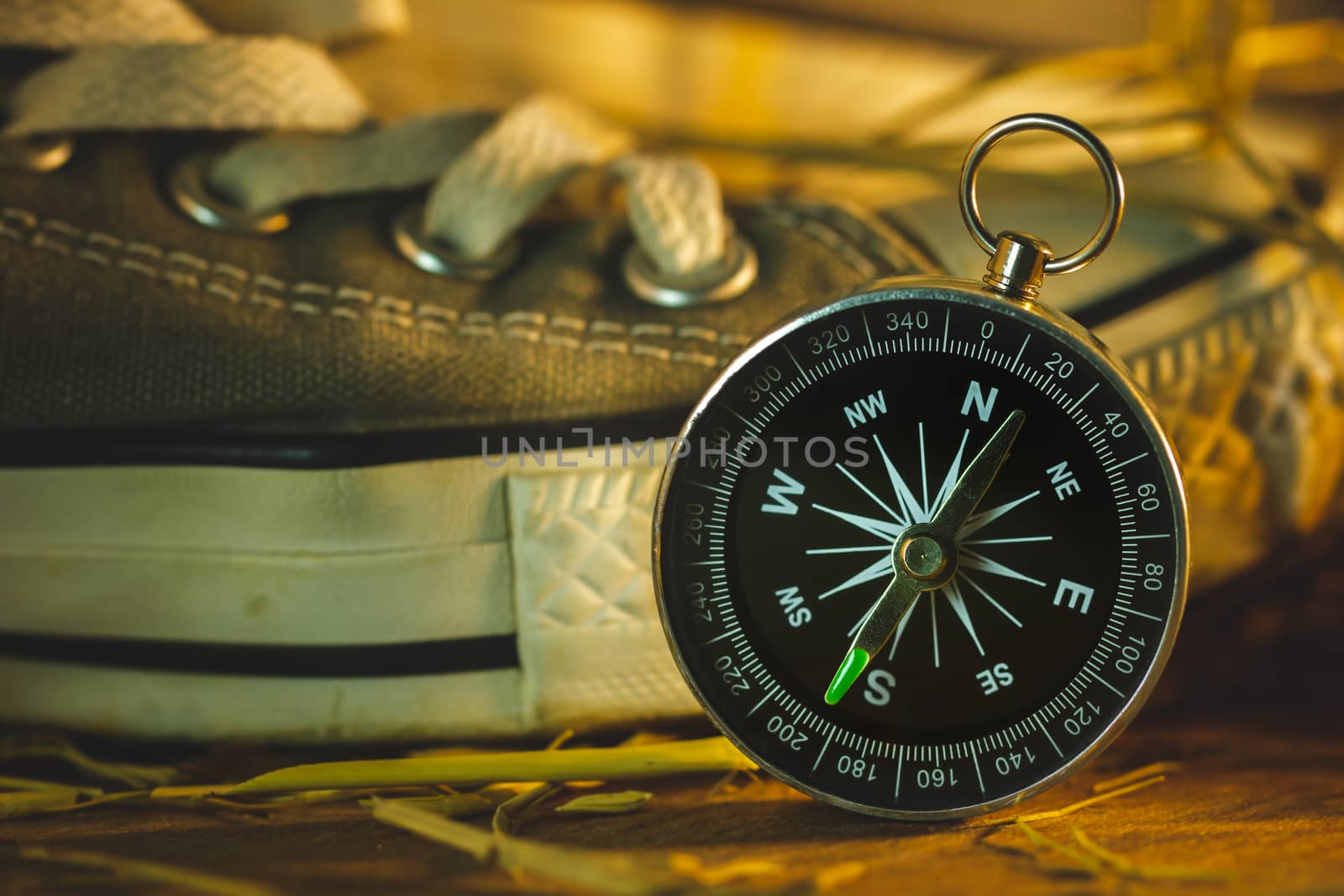 Compass and sneakers with pine flowers and dry wheat straw on wooden table in morning sunlight. Concept of adventure tourism or survival in the forest.