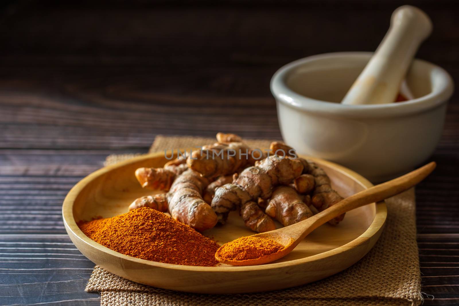 Turmeric powder and turmeric root on wooden dish with mortar and pestle on hemp mat in morning sunlight. Concepts of herbal medicine and health care.