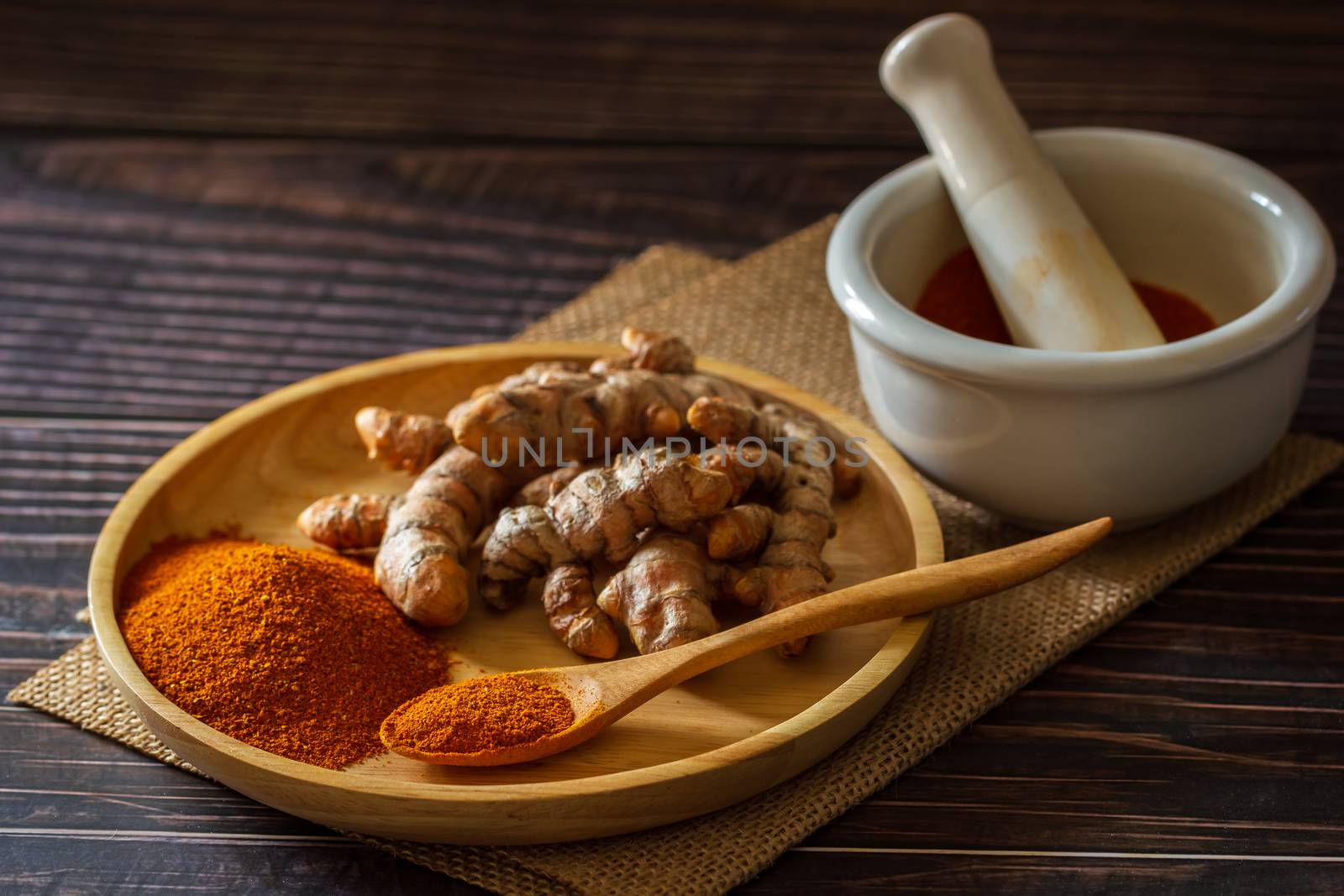 Turmeric powder and turmeric root on wooden dish with mortar and pestle on hemp mat in morning sunlight. Concepts of herbal medicine and health care.