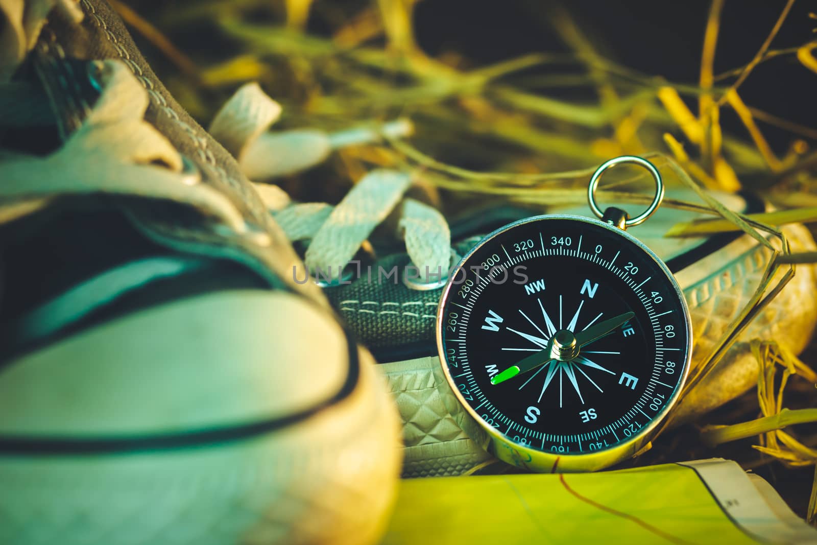 Compass and paper maps with sneakers and pine flowers placed on dry wheat straw in morning sunlight. Concept of adventure tourism or survival in the forest.