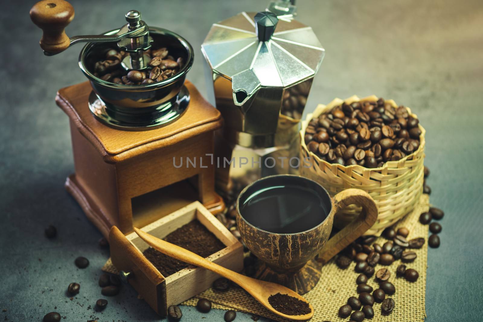 Brew black coffee in coconut cup and morning lighting. Roasted coffee beans in a bamboo basket and wooden spoon. Vintage coffee grinder and moka pot. Concept of coffee time in morning or start the new day.