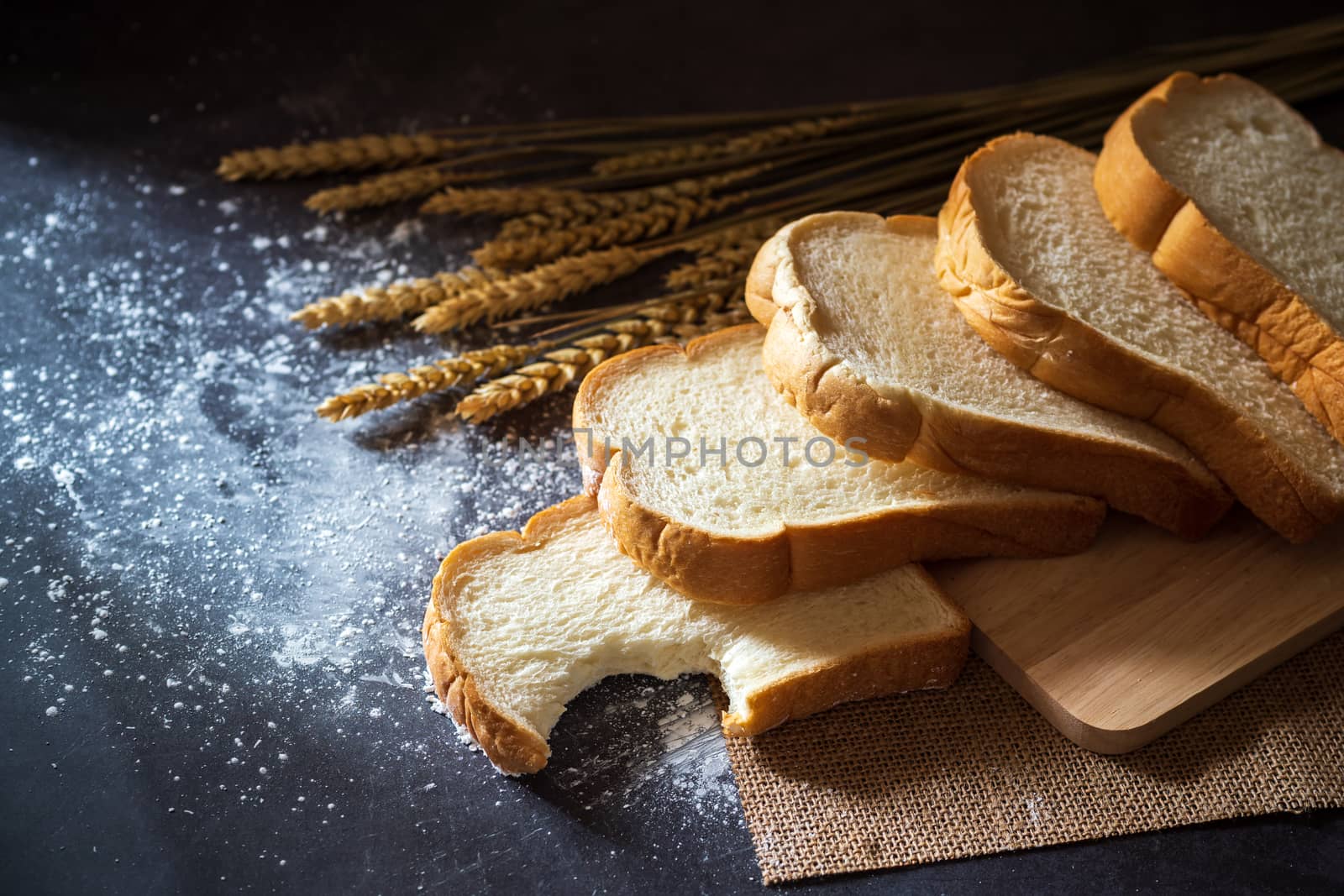 Bread on a wooden cutting board and the wheat grains placed besi by SaitanSainam