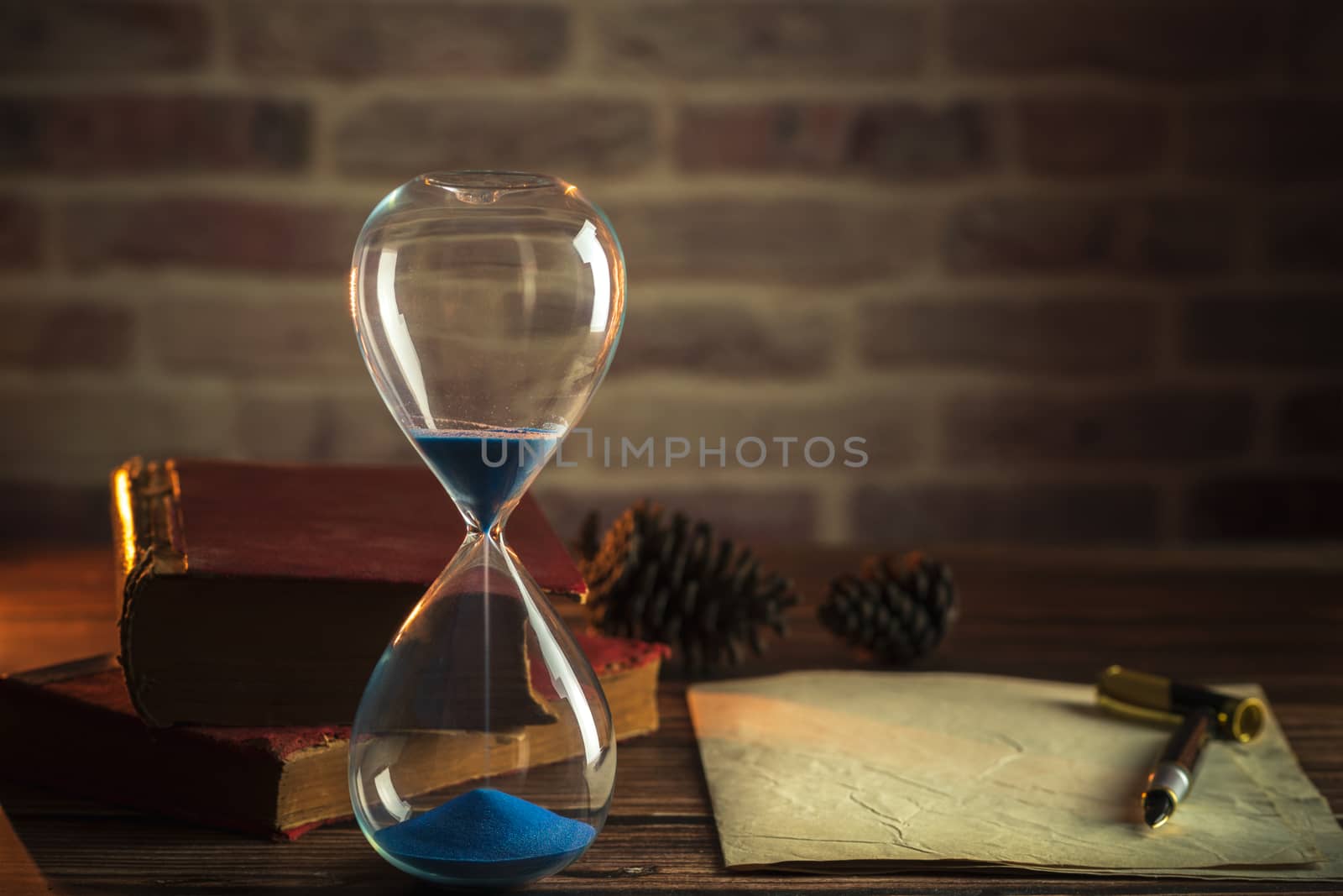 Hourglass and old books with old paper and pen on wooden tables in lighting of the lantern.