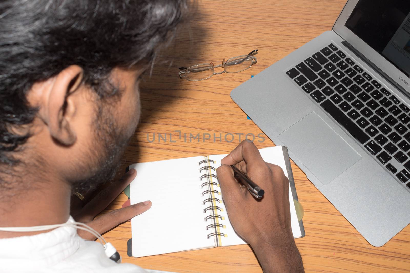 Businessman writing in his diary. Open notebook with blank pages next to cup of coffee and eyeglasses on wooden table. Business still life concept with office stuff on table. Top view with copy space. by sudiptabhowmick