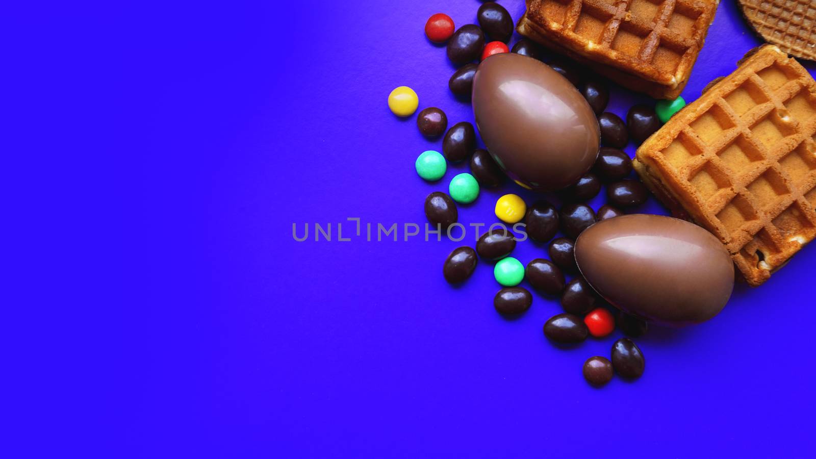 Delicious chocolate easter eggs, waffles, sweets on dark blue background