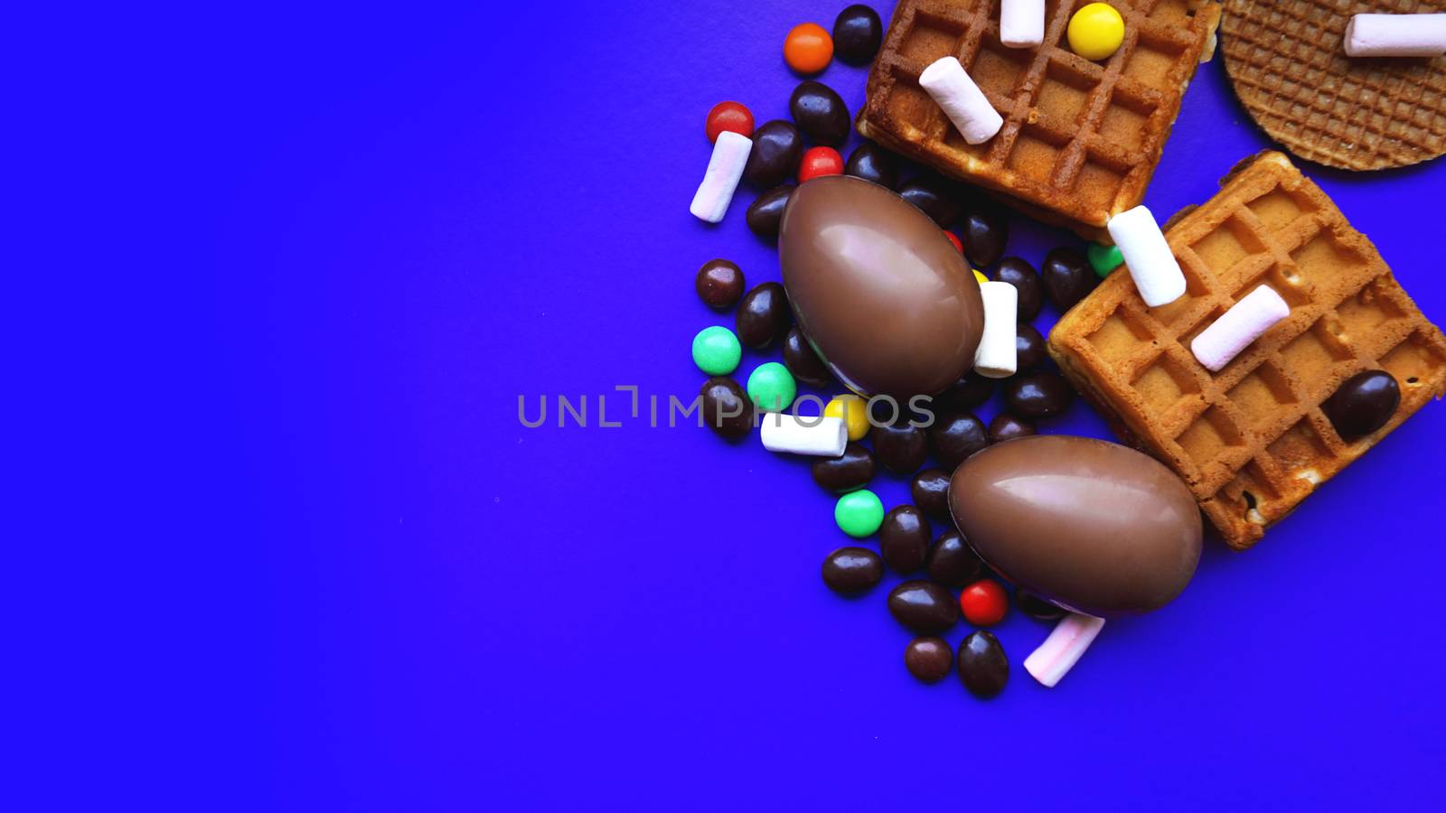 Delicious chocolate easter eggs, waffles, sweets on dark blue background