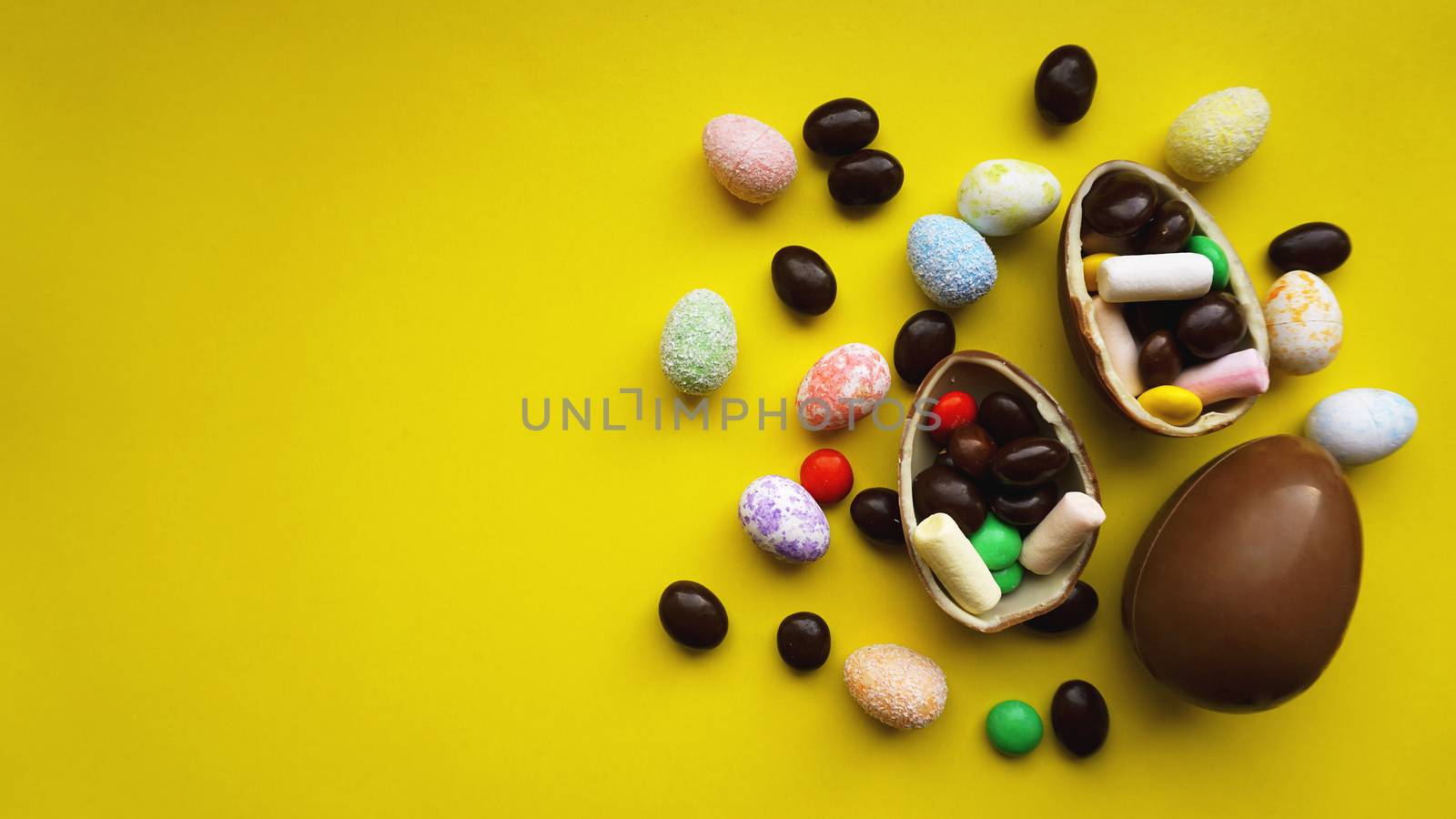 Delicious chocolate easter eggs, sweets on bright yellow background