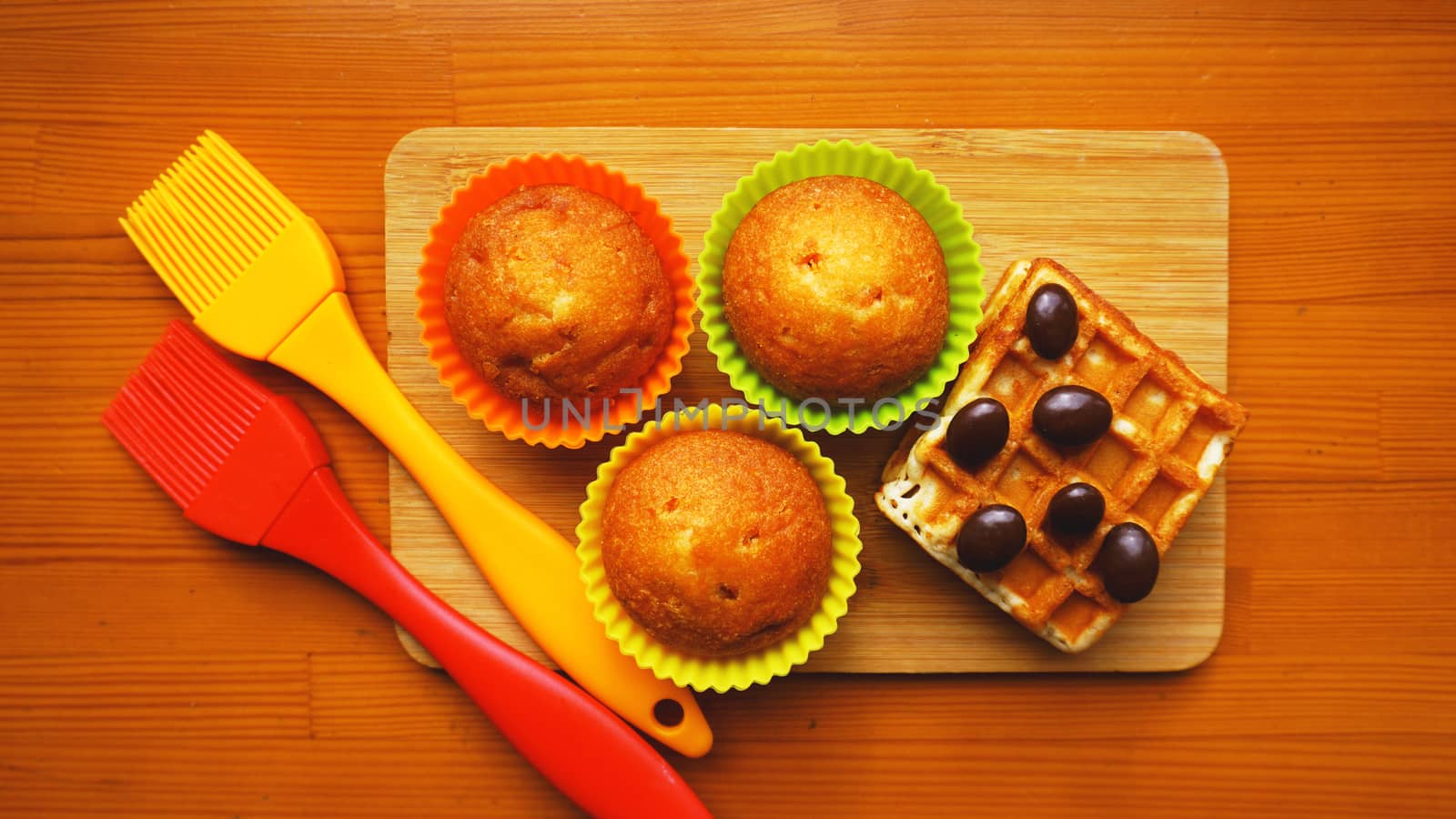 Simple mini muffins in colorful silicone bakeware and waffles. Kitchen and cooking concept on wooden background