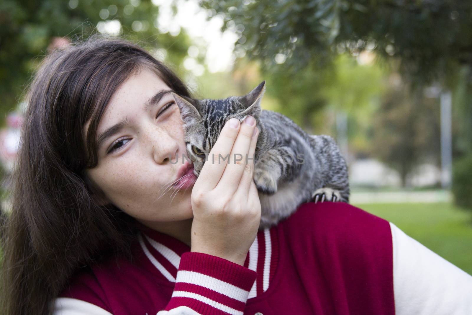 Autumn sunny photo of a teenage girl hugging her cat, close-up, outdoor photo on a green background