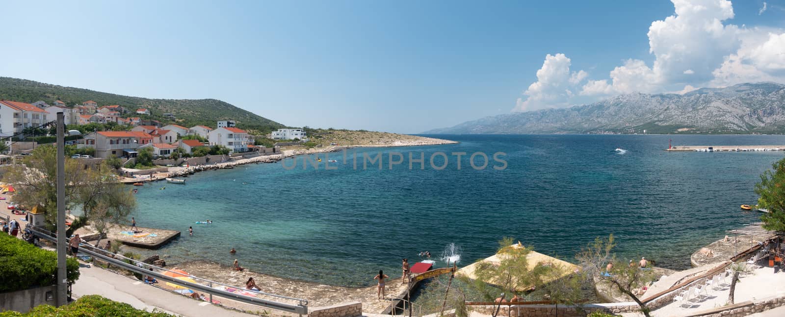 Beach in small village Vinjerac near Zadar, Croatia, people bathing in turquoise blue water in the lagoon and beautiful panorama view on Velebit mountain with Paklenica national park, summer time