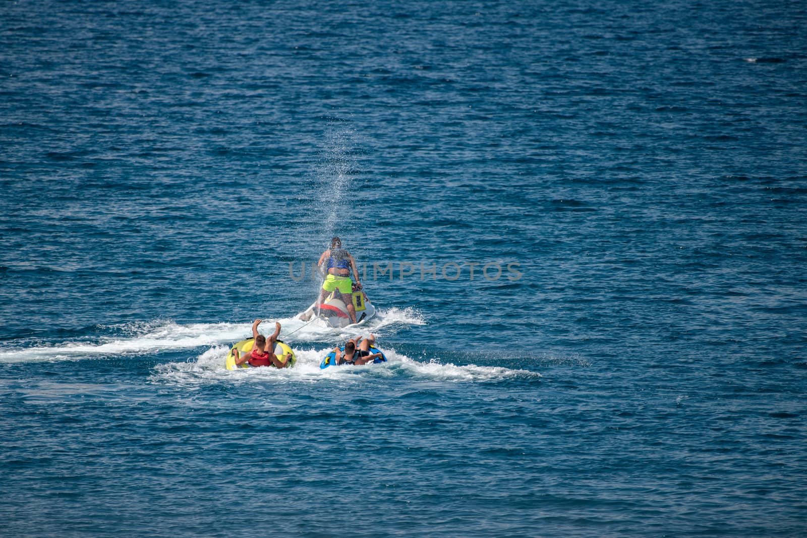 Jet ski pulling two tubes in water, water sports and fun in summer at beach, travel and vacation fun, water spraying all directions