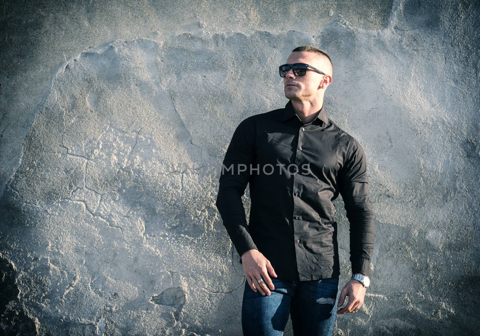 One handsome young man in urban setting in European city, standing, wearing black jacket and jeans