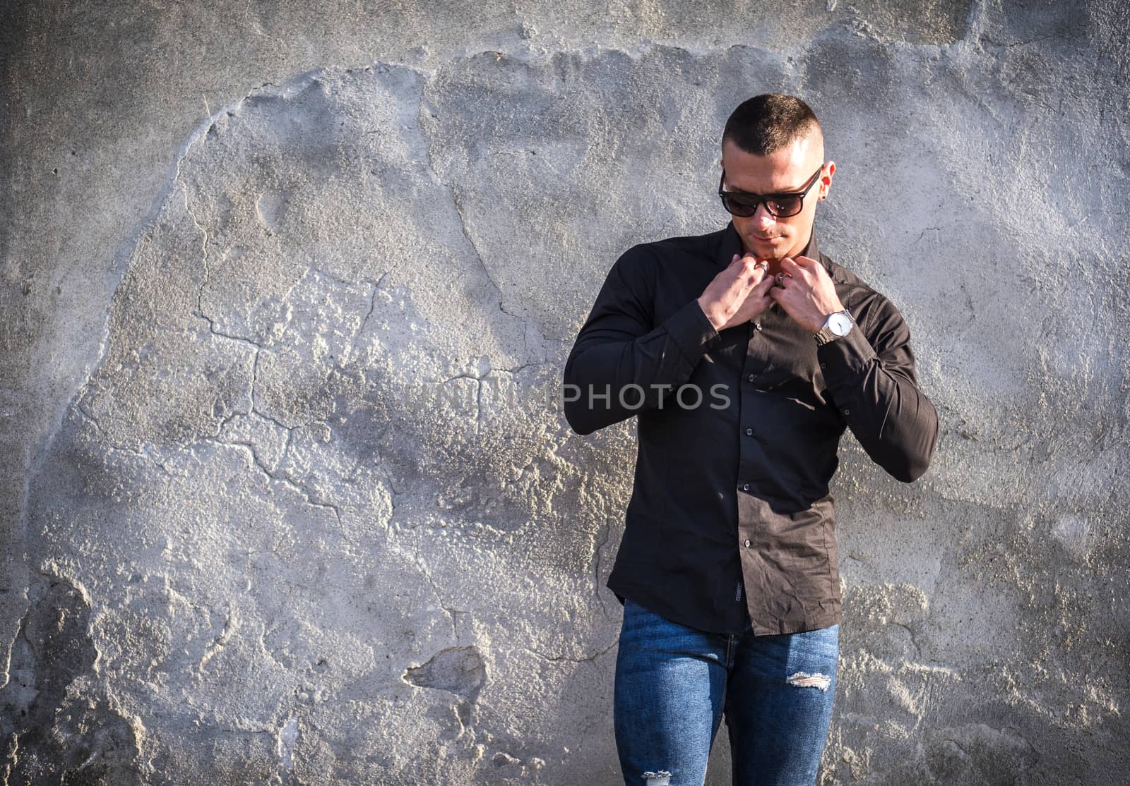 One handsome young man in urban setting in European city, standing, wearing black jacket and jeans