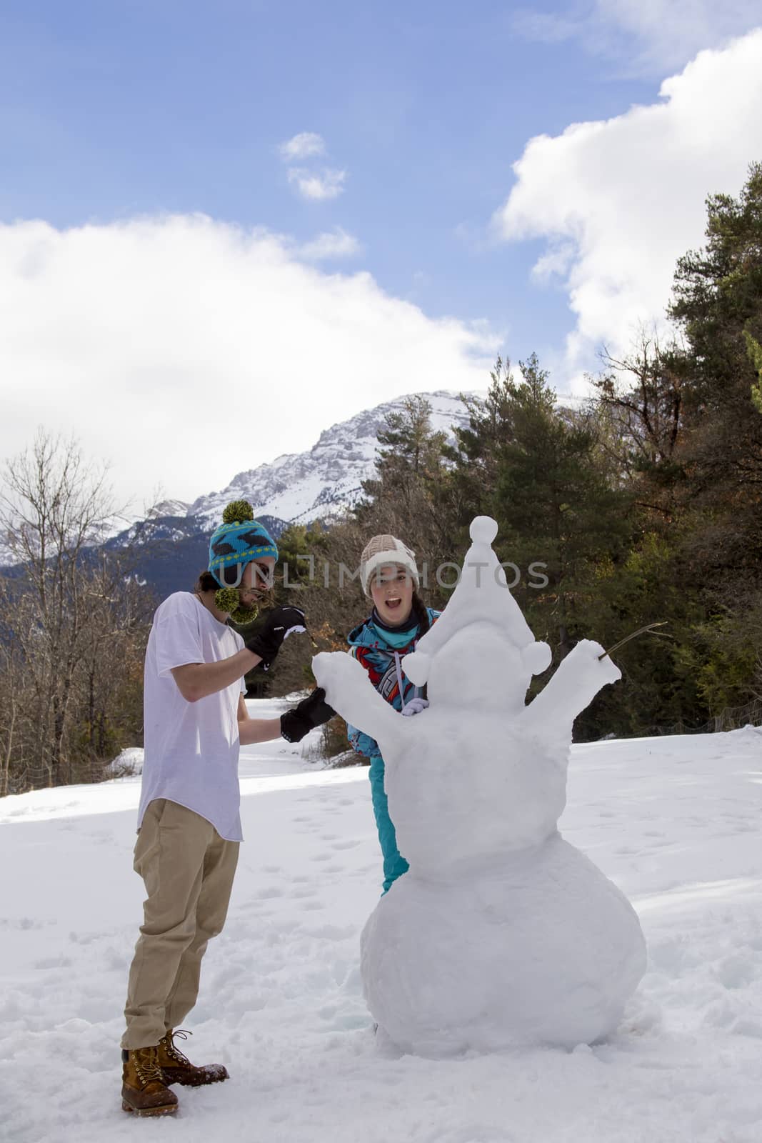 A young couple together make a snowman in the winter forest in the mountains. by Anelik