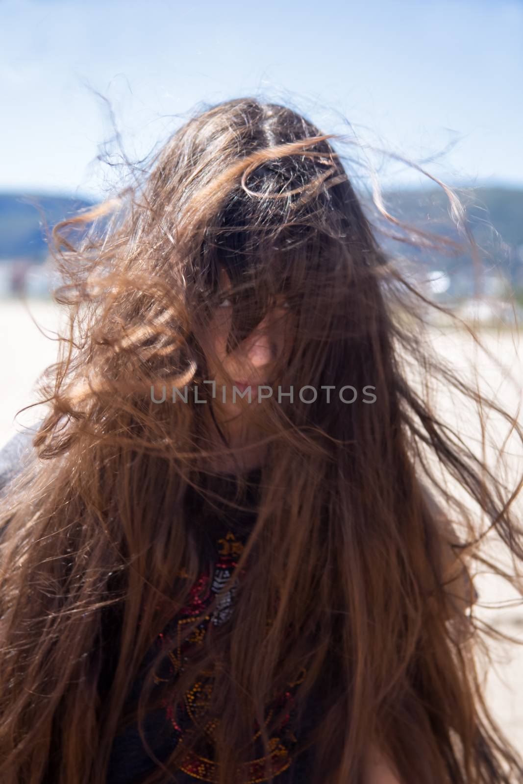 Portrait of brunette girl with long flying hair in the wind outdoors. Young casual woman with wavy hair covering her face. Teenage girl with messy windy tousy blowsy hair.