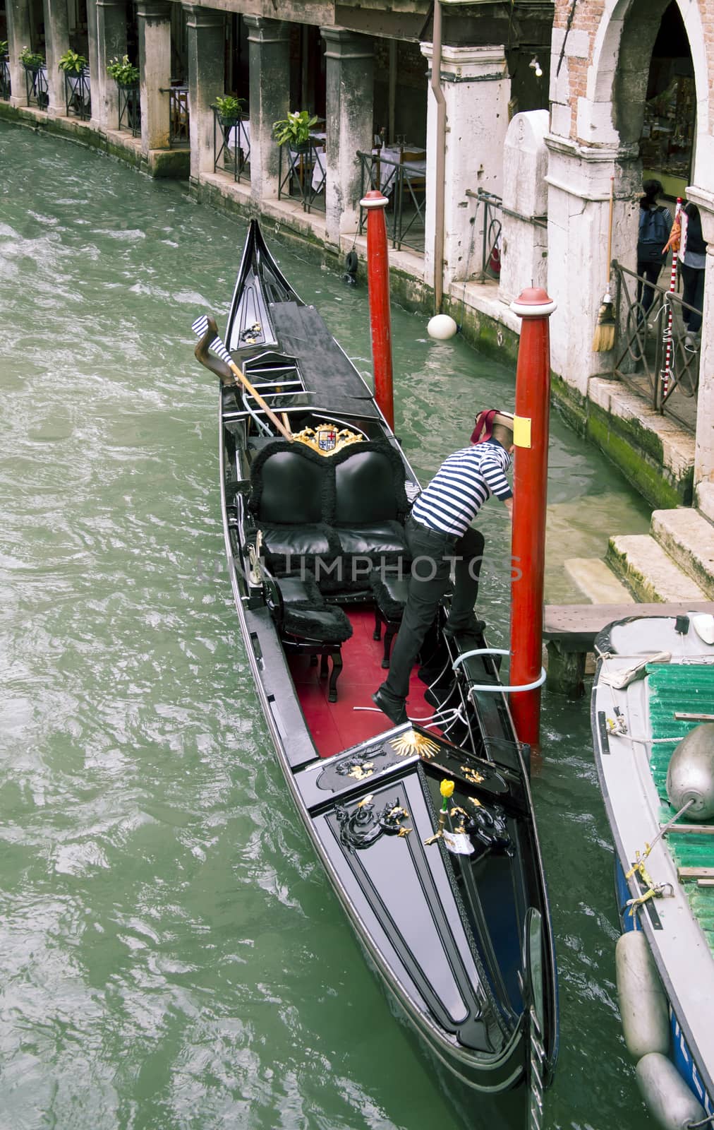 Man mooring gondola near stone steps in blue clear water of channel water
