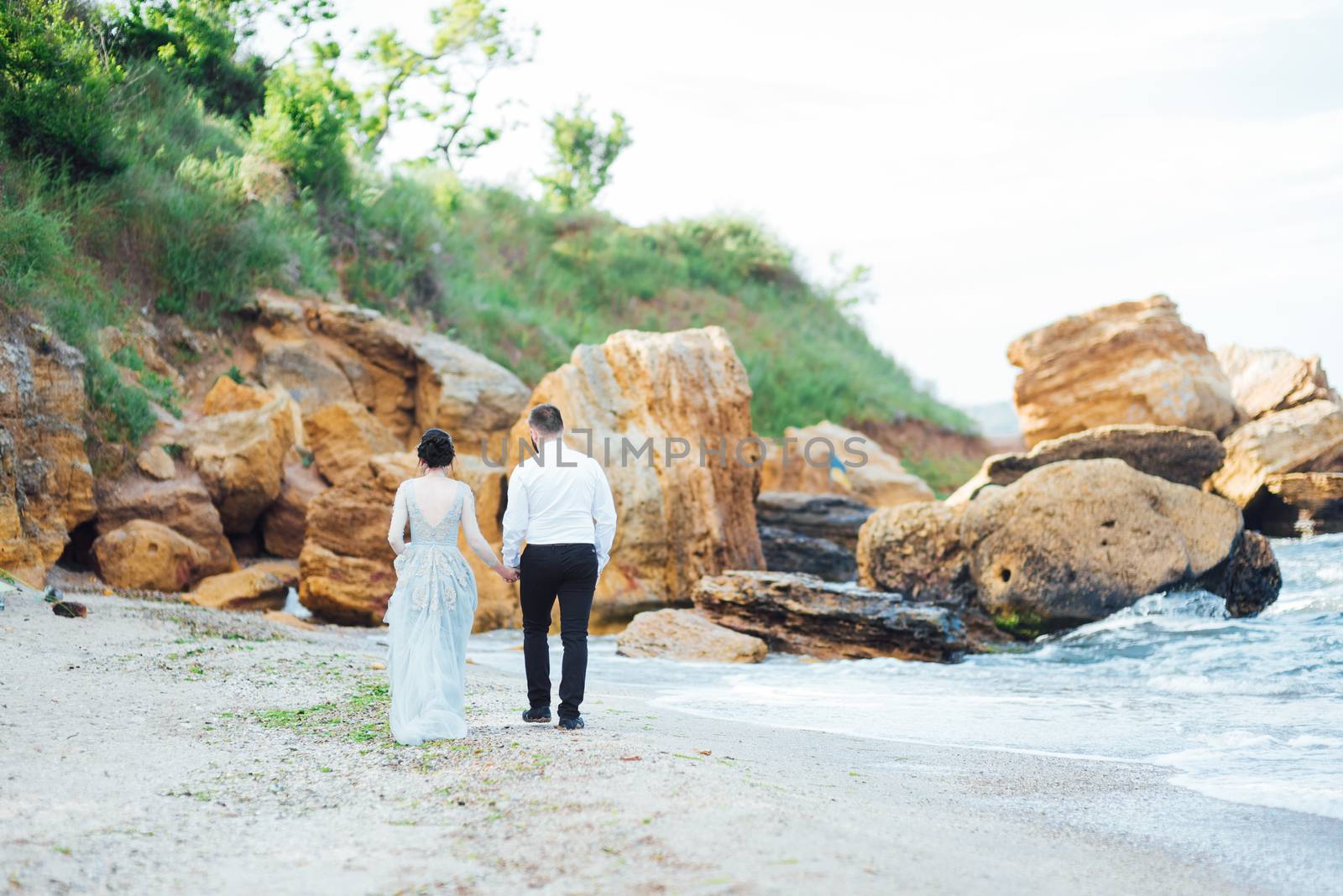 same couple with a bride in a blue dress walk along the ocean shore