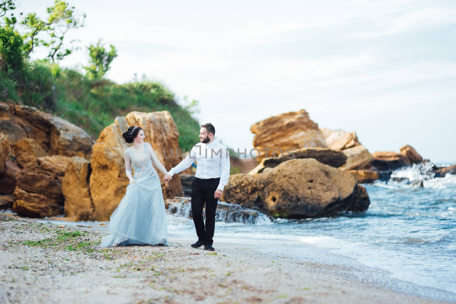 same couple with a bride in a blue dress walk along the ocean shore