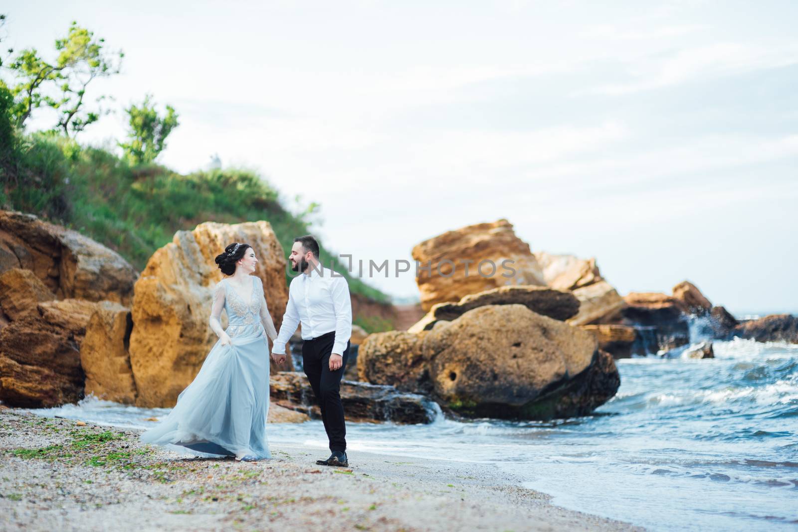 same couple with a bride in a blue dress walk along the ocean shore