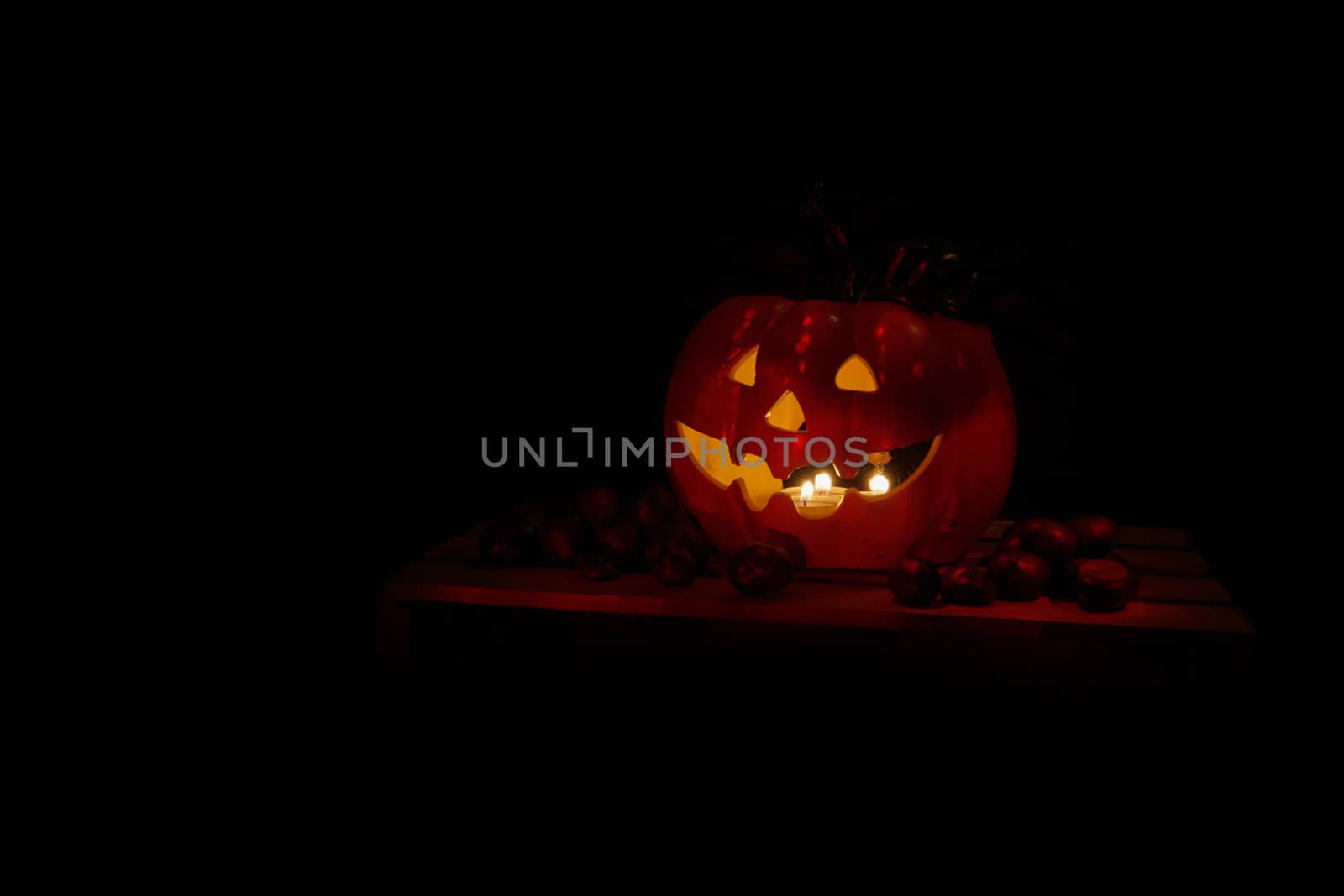 Halloween Pumpkin od dark background with chestnuts, illuminated by candles, dark red glow on black, isolated with copyspace, holiday concept, decoration