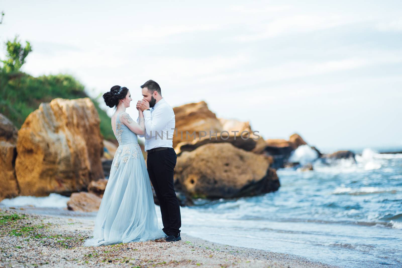 same couple with a bride in a blue dress walk along the ocean shore