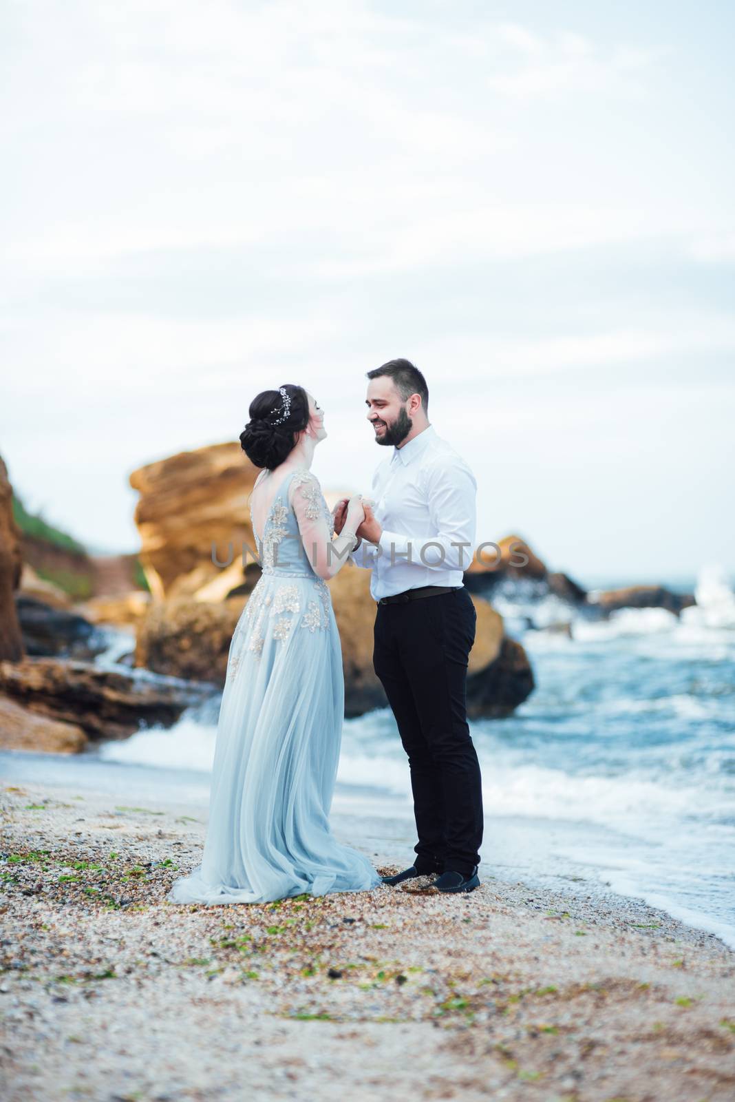 same couple with a bride in a blue dress walk along the ocean shore