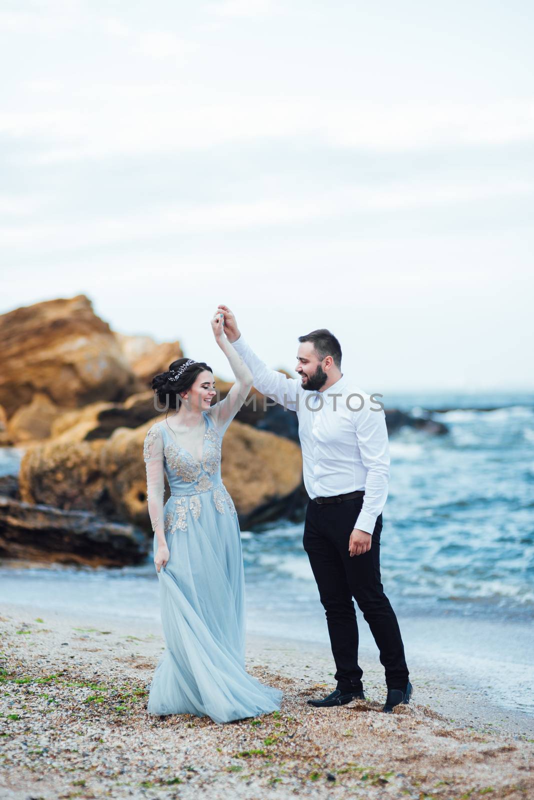 same couple with a bride in a blue dress walk along the ocean shore