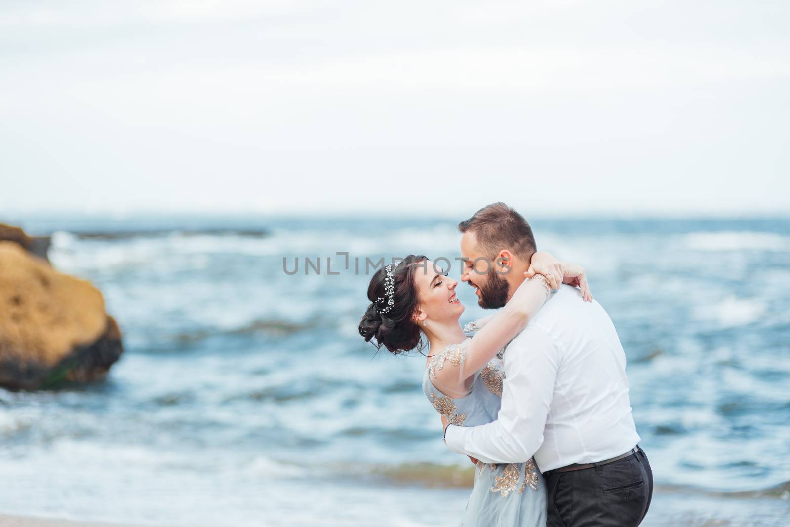 same couple with a bride in a blue dress walk along the ocean shore