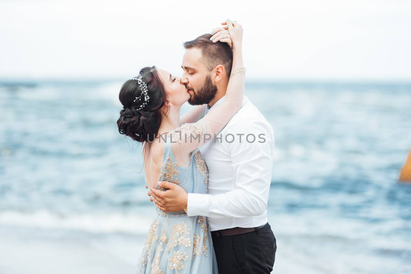 same couple with a bride in a blue dress walk along the ocean shore